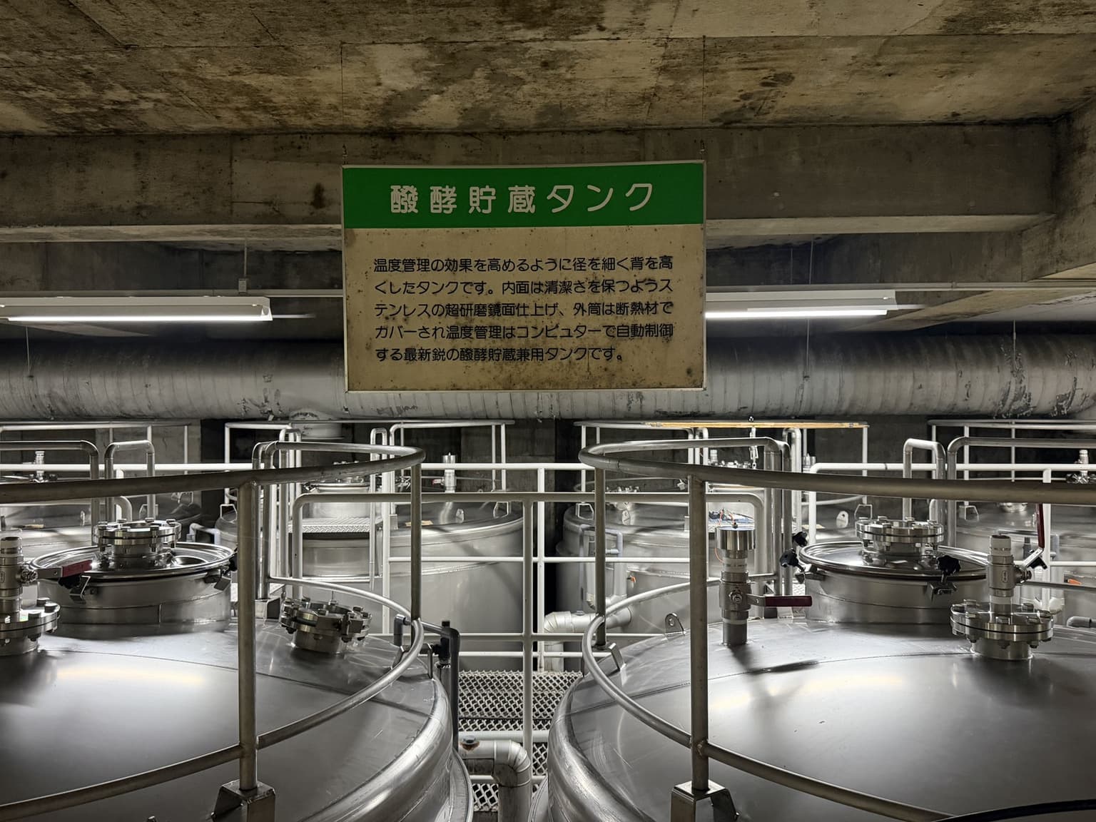 シャトー酒折の醗酵貯蔵タンクの案内板と並んだステンレスタンク