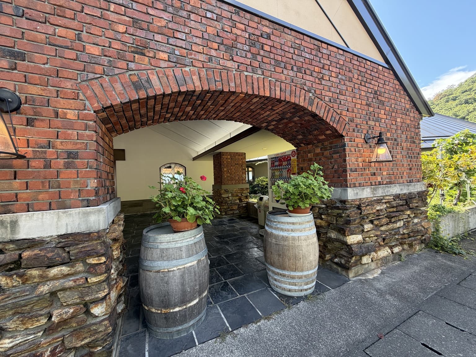 シャトー酒折ワイナリーの赤レンガのアーチと入口に置かれた木樽や鉢植え